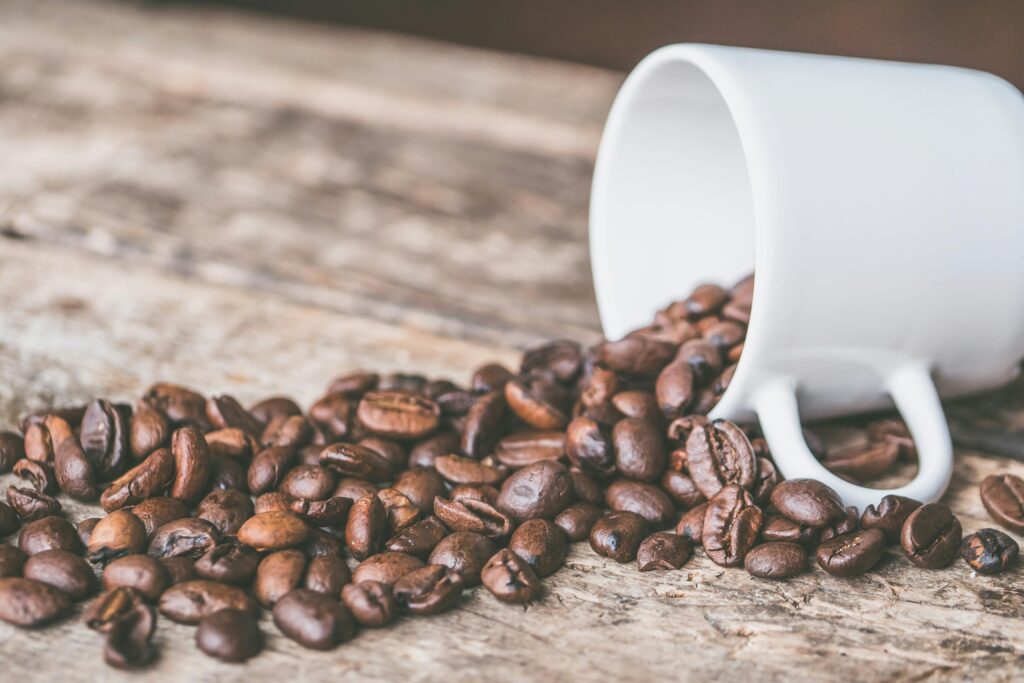 pexels-photo-606545-606545 Coffee beans spilling from a white mug on a rustic wooden surface, embodying a cozy and warm atmosphere.